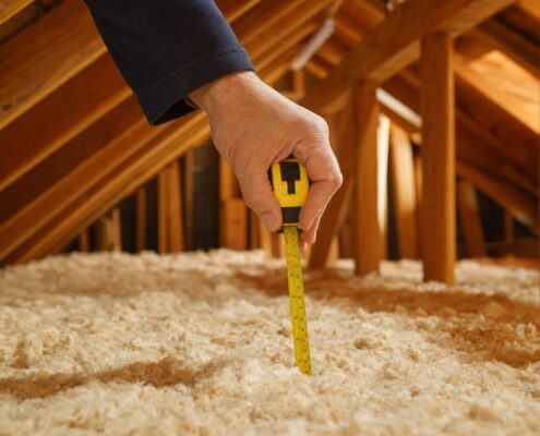 Hand measuring loft insulation depth with a yellow tape measure, illustrating how to prepare for an EPC assessment
