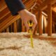 Hand measuring loft insulation depth with a yellow tape measure, illustrating how to prepare for an EPC assessment
